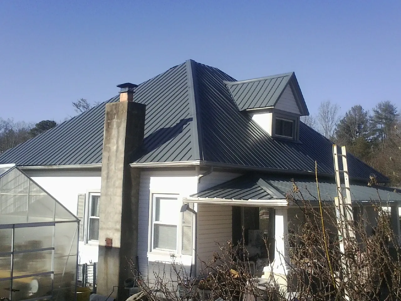 Dark blue standing seam metal roof on a white farmhouse with dormer — Slate & Tile Roof Repair by Roofing Brothers in Salamanca