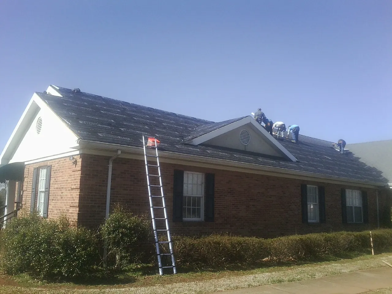 Crew tearing shingles off a brick ranch roof with a ladder set — Metal Roof Repair work by our crew in Salamanca