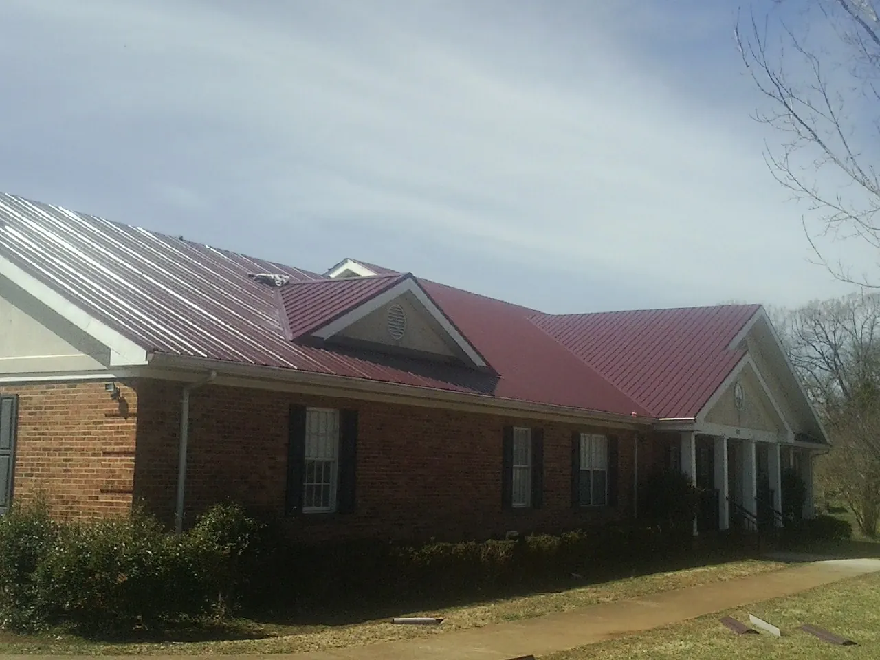Red metal roof with gabled entries on a long brick building, from a Hail Damage Roof Repair job in Salamanca