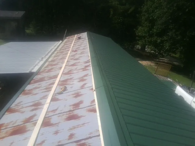 Old rusted panels beside newly installed green metal roofing — Wind Damage Roof Repair by Roofing Brothers in Salamanca
