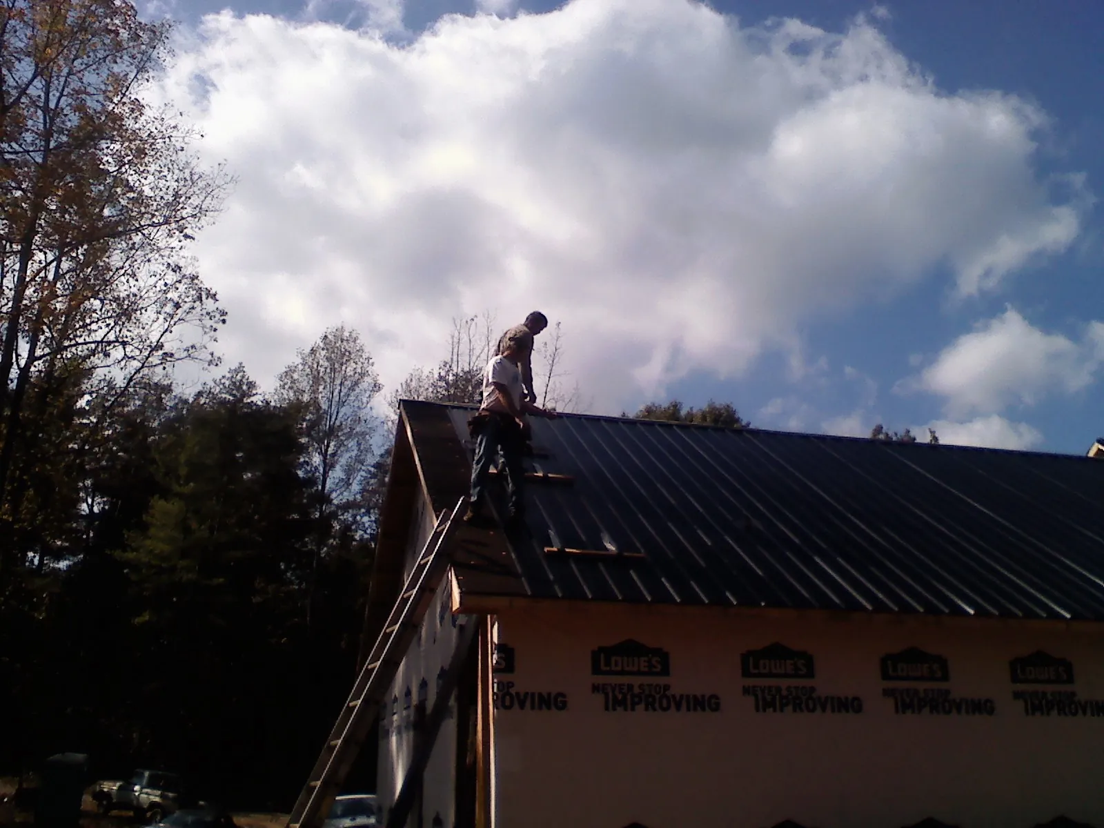 Roofer fastening dark metal panels high against a cloudy sky, from a Roof Inspection job in Salamanca