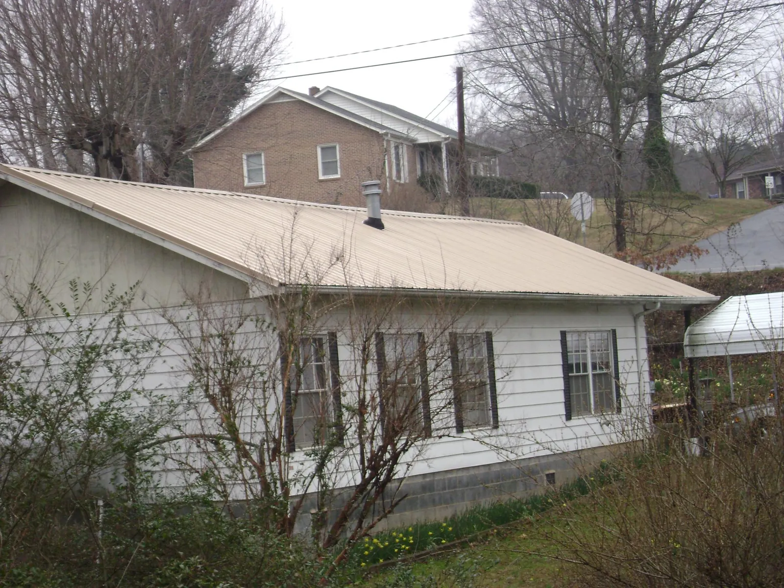 Tan metal roof on a white sided house set into a hillside — Commercial Roofing by Roofing Brothers in Salamanca