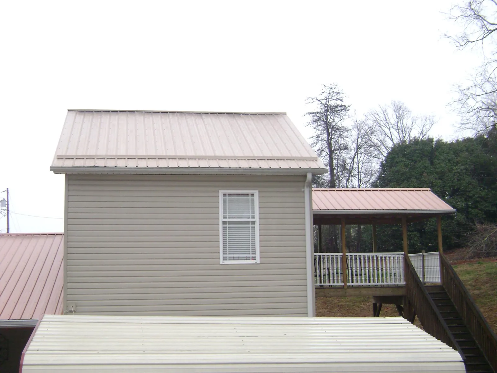 Tan metal roofs on a two story addition and attached porch, from a Roof Replacement job in Salamanca